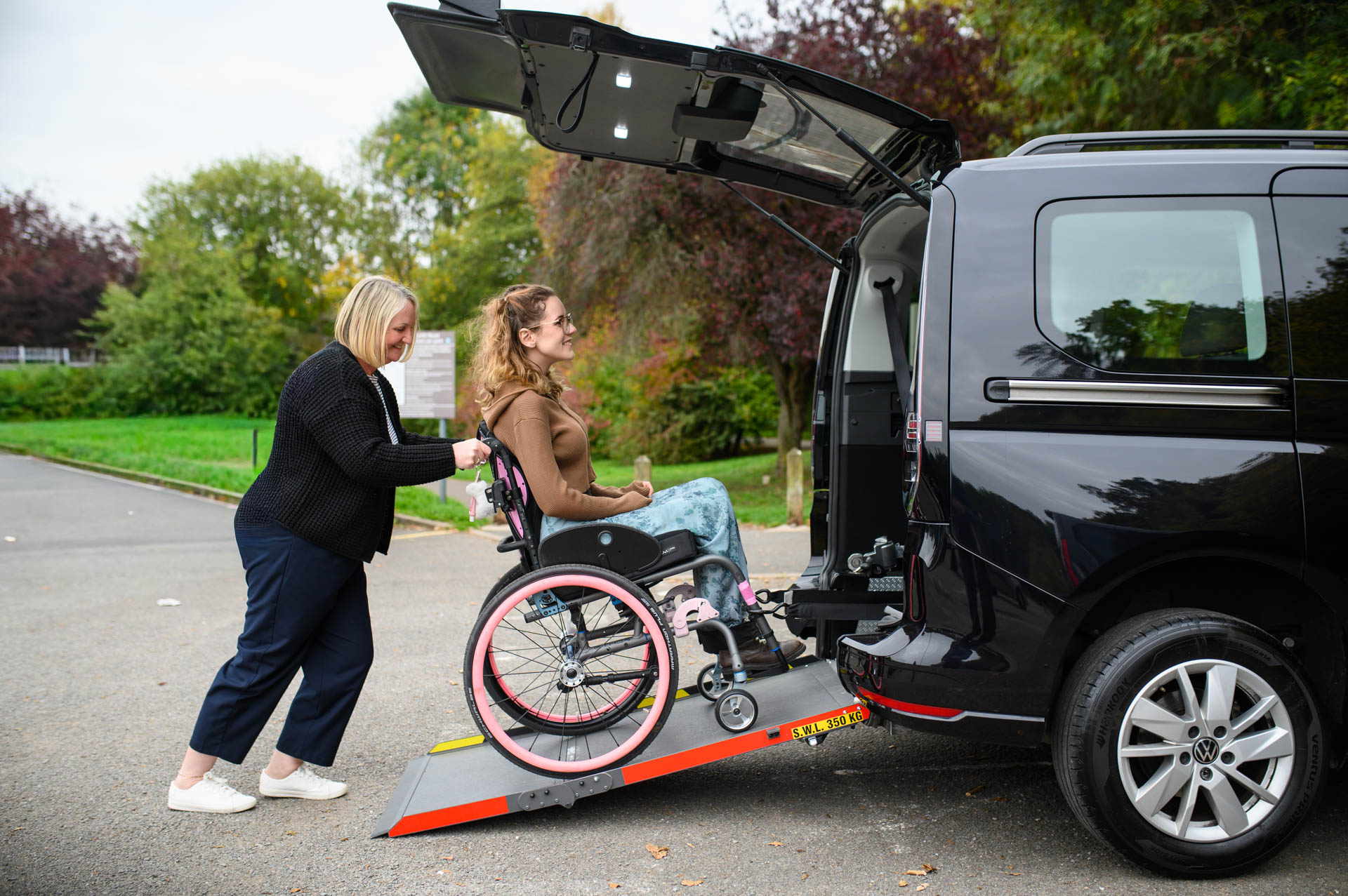 Wav hire cost – carer helping a wheelchair user up the ramp of a wheelchair accessible vehicle